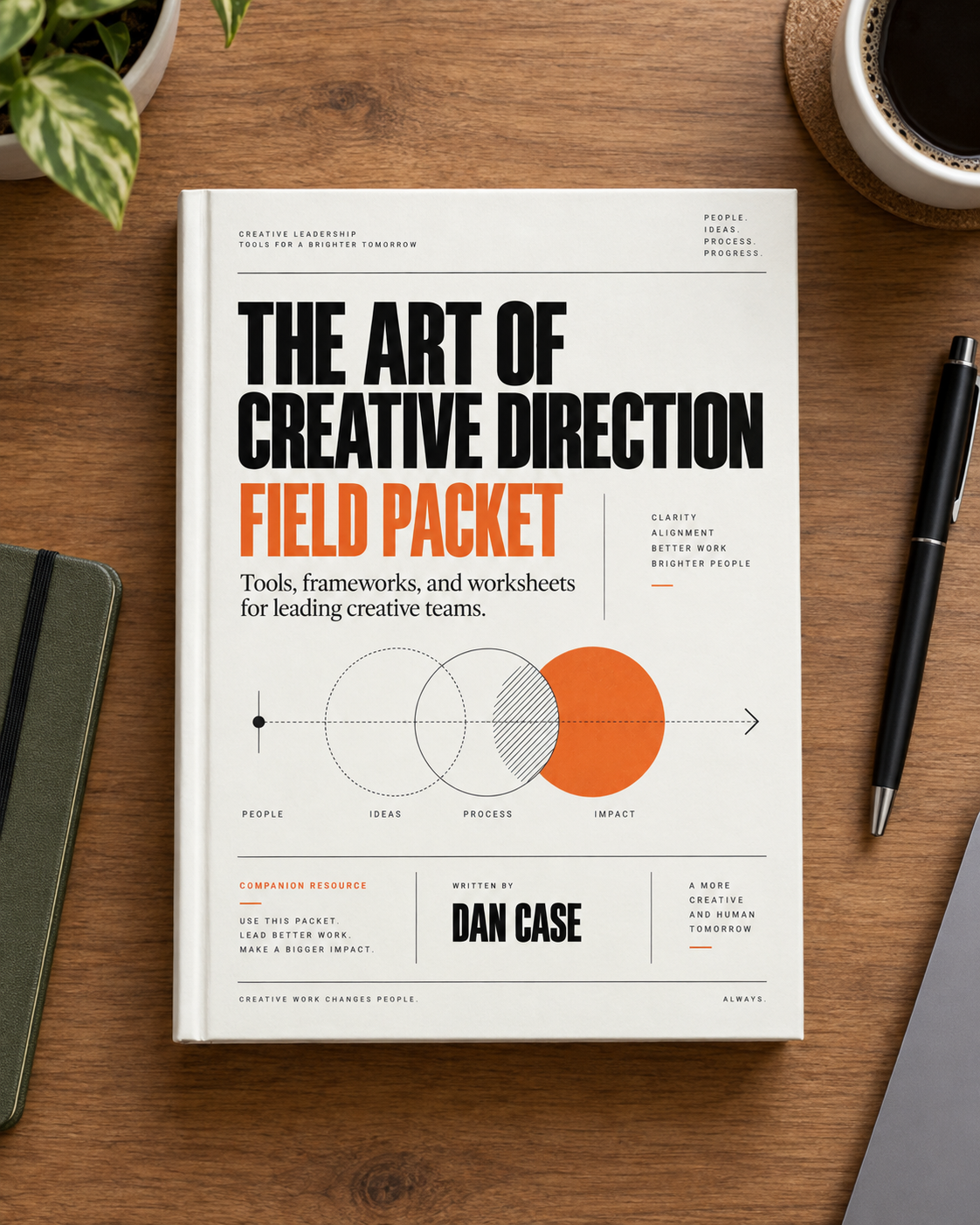 The Art of Creative Direction Field Packet by Dan Case, lying on a wooden desk beside a coffee cup, notebook, and pen